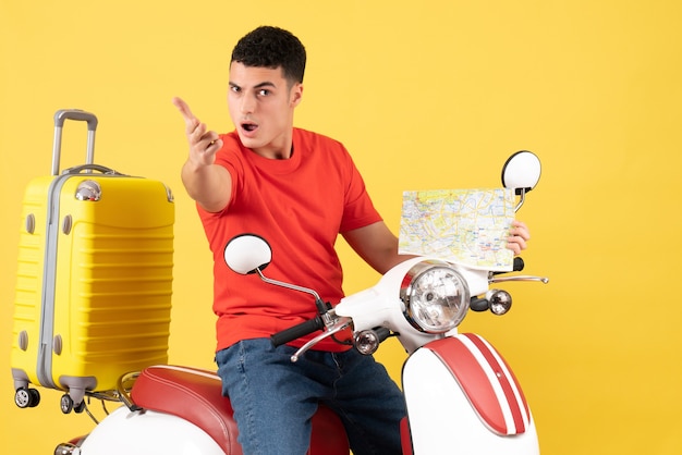 Vista frontal joven en ropa casual en ciclomotor con mapa de viaje que alcanza la mano