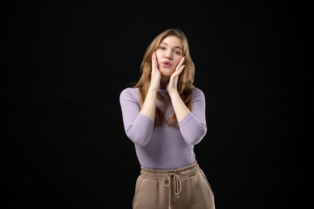 Vista frontal de la joven rubia poniendo sus manos en las mejillas en la oscuridad