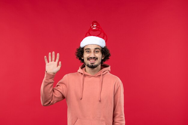 Vista frontal del joven saludando y sonriendo en la pared roja