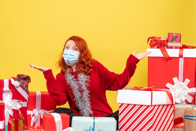 Vista frontal joven sentado alrededor de regalos de Navidad en máscara en amarillo