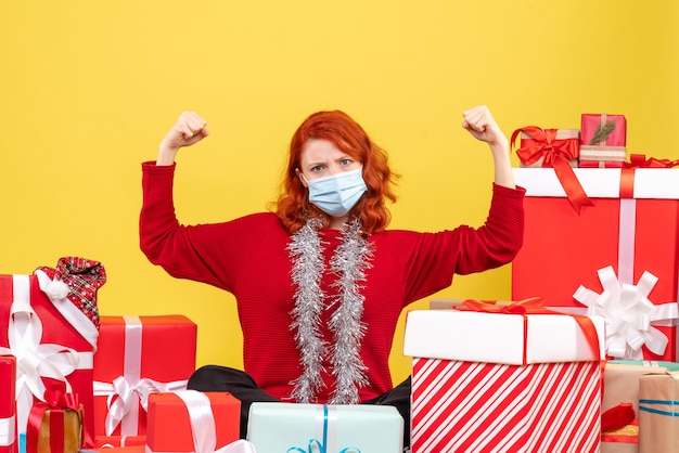 Vista frontal joven sentado alrededor de regalos de Navidad en máscara en amarillo