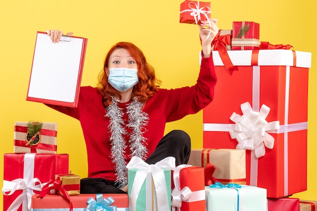 Vista frontal joven sentado alrededor de regalos de Navidad con nota de archivo en amarillo