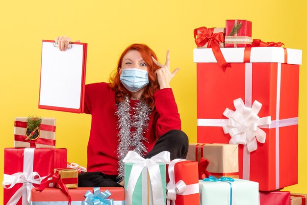 Vista frontal joven sentado alrededor de regalos de Navidad con nota de archivo en amarillo