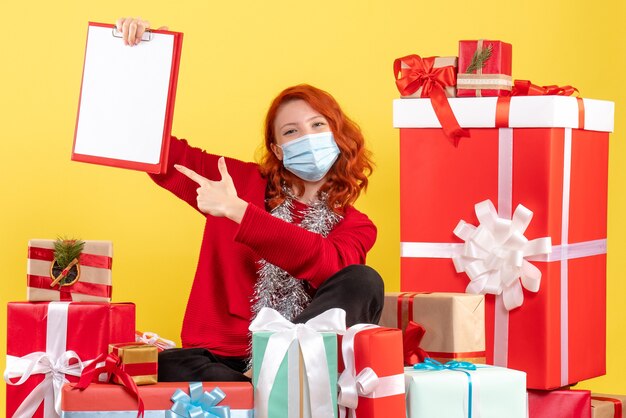 Vista frontal joven sentado alrededor de regalos de Navidad con nota de archivo en amarillo