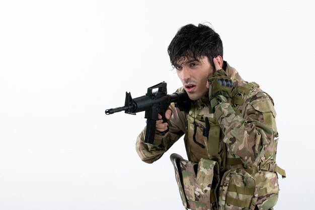 Vista frontal del joven soldado en camuflaje con ametralladora pared blanca