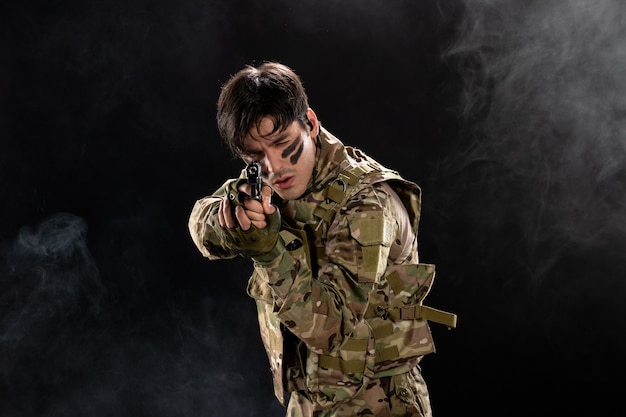 Foto gratuita vista frontal del joven soldado de camuflaje con el objetivo de pistola en la pared negra