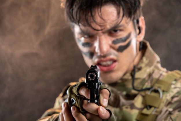 Vista frontal del joven soldado de camuflaje con el objetivo de pistola en la pared negra