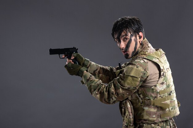 Vista frontal del joven soldado en camuflaje con el objetivo de pistola en el piso oscuro de la guerra de tanques de Palestina