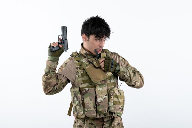 Vista frontal del joven soldado en camuflaje con pistola pared blanca