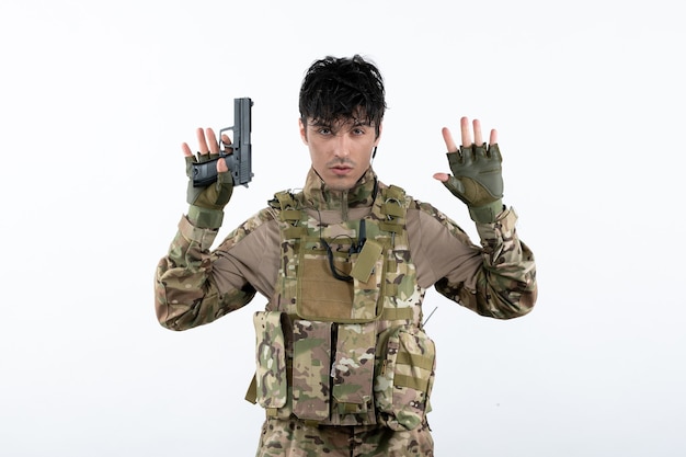 Vista frontal del joven soldado en camuflaje con pistola pared blanca