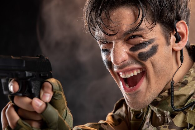 Vista frontal del joven soldado de camuflaje con pistola en pared negra