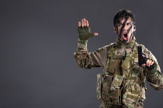 Foto gratuita vista frontal del joven soldado de camuflaje con pistola en la pared oscura