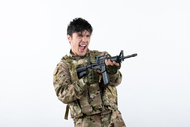 Vista frontal del joven soldado luchando con ametralladora pared blanca