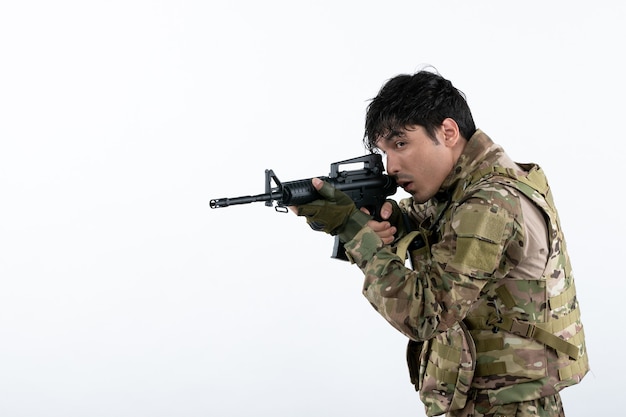 Vista frontal joven soldado luchando en camuflaje con ametralladora pared blanca