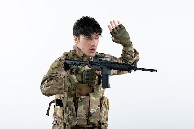 Vista frontal joven soldado luchando en camuflaje con ametralladora pared blanca