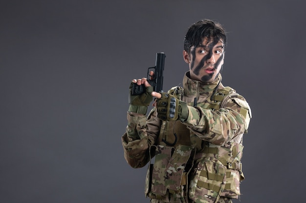 Vista frontal joven soldado surrending en camuflaje con pistola en pared oscura