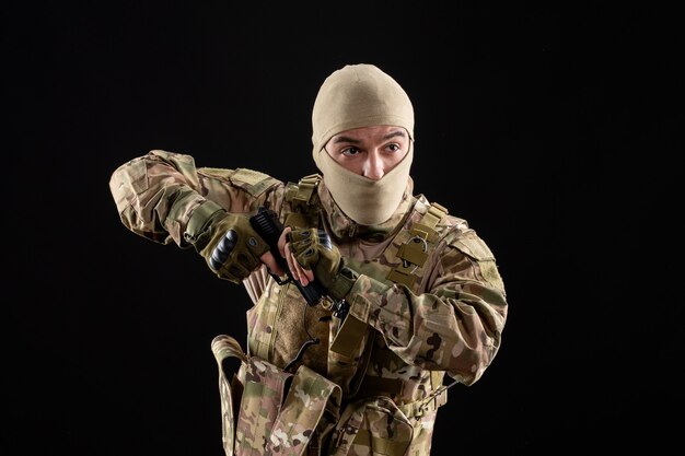 Vista frontal del joven soldado en uniforme y máscara en la pared negra