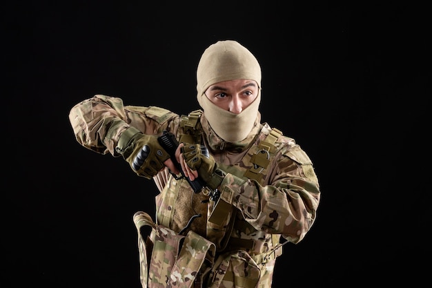 Vista frontal del joven soldado en uniforme y máscara en la pared negra