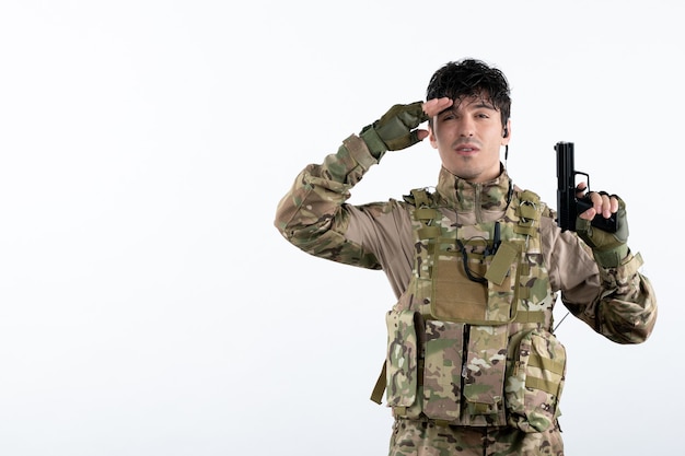Vista frontal joven soldado en uniforme militar con pistola pared blanca
