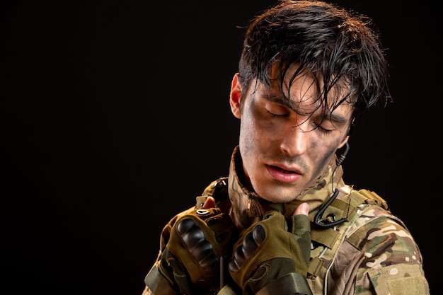 Vista frontal del joven soldado en uniforme en la pared oscura