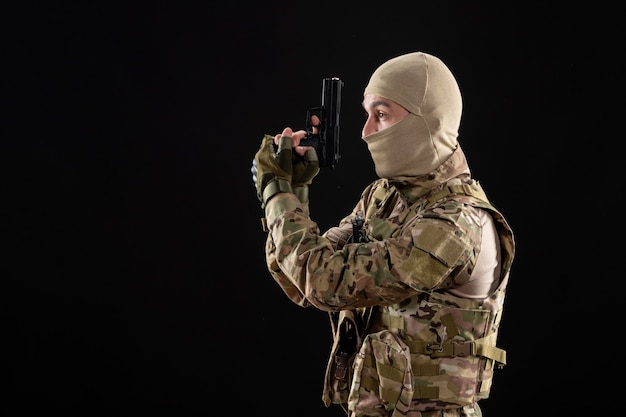 Vista frontal joven soldado en uniforme con pistola en pared negra