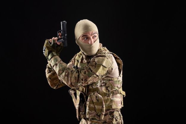 Vista frontal joven soldado en uniforme con pistola en pared negra