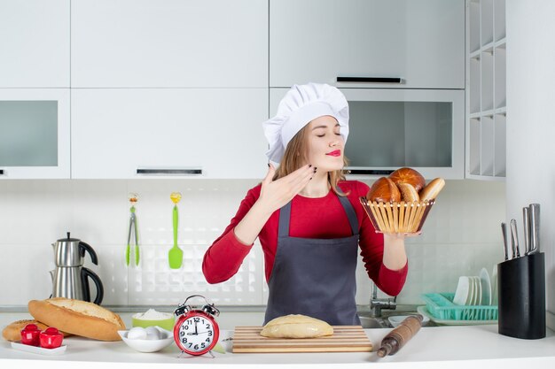 Vista frontal joven con sombrero de cocinero y delantal oliendo pan en la cocina