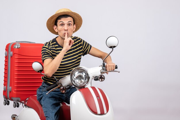 Vista frontal del joven con sombrero de paja en ciclomotor haciendo señal de silencio