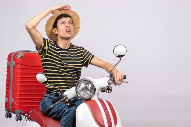 Vista frontal del joven con sombrero de paja en ciclomotor mirando hacia arriba