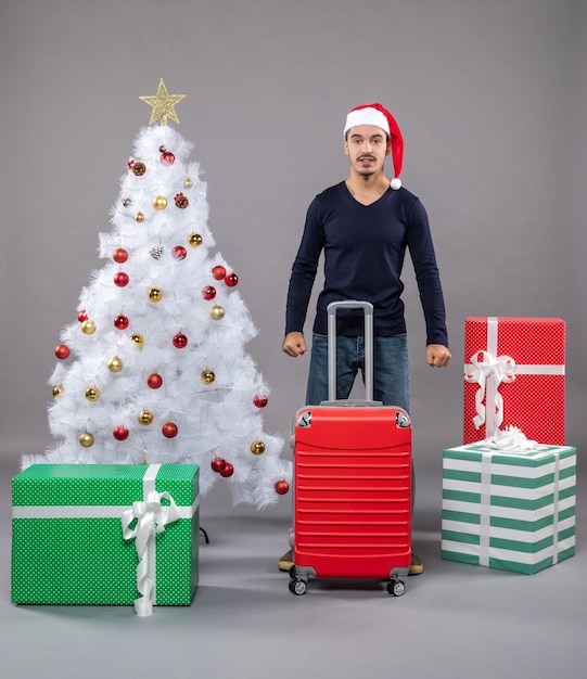 Vista frontal joven con sombrero de santa de pie cerca del árbol de Navidad en aislado