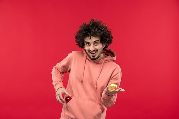 Vista frontal del joven sonriendo con juguetes de navidad en la pared roja