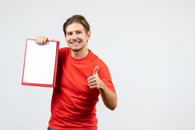 Vista frontal del joven sonriente en blusa roja sosteniendo documento haciendo gesto ok sobre fondo blanco.