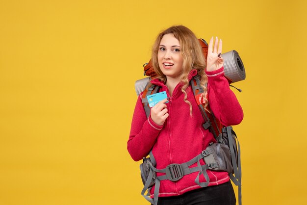 Vista frontal de la joven sonriente viajera en máscara médica recogiendo su equipaje y mostrando tres