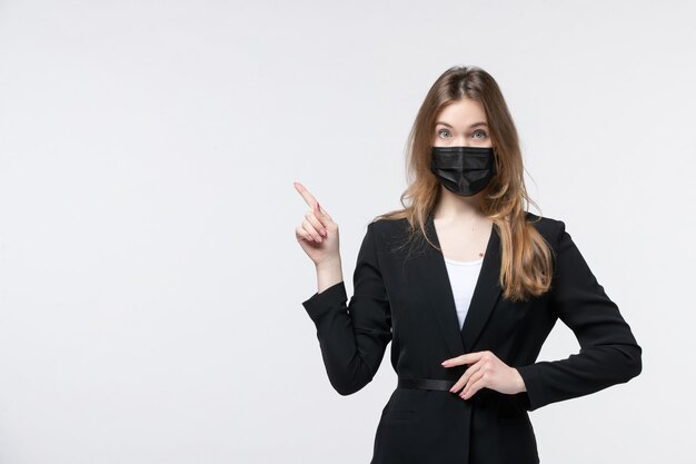 Vista frontal de la joven sorprendida en traje con mascarilla quirúrgica y apuntando hacia arriba en blanco