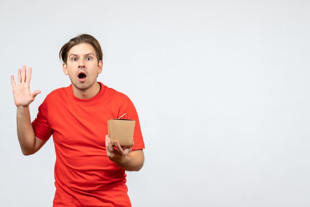 Vista frontal del joven sorprendido en blusa roja sosteniendo una pequeña caja y mostrando cinco sobre fondo blanco.