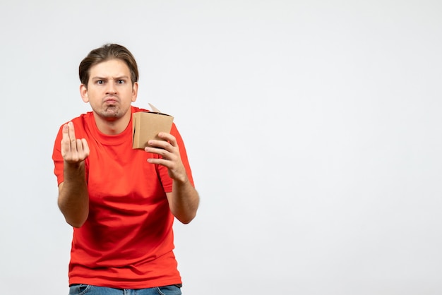 Vista frontal del joven sorprendido en blusa roja sosteniendo una pequeña caja sobre fondo blanco.