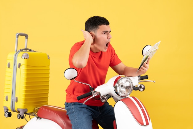 Vista frontal joven sorprendido en ciclomotor mirando el mapa en amarillo