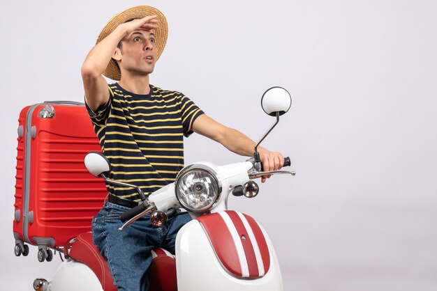 Vista frontal del joven sorprendido con sombrero de paja en ciclomotor mirando algo