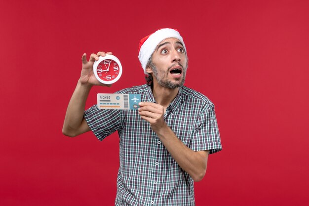 Vista frontal joven sosteniendo billete y reloj en pared roja vuelo rojo emoción tiempo