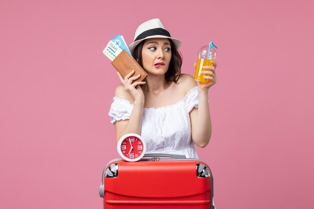 Vista frontal joven sosteniendo boletos y cócteles de vacaciones en el piso rosa viaje mujer viaje de vacaciones calor de verano