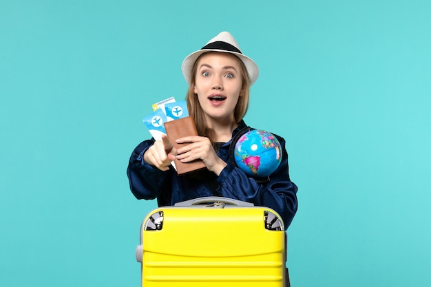 Vista frontal joven sosteniendo boletos y globo sobre fondo azul claro viaje en avión viaje de vacaciones por mar