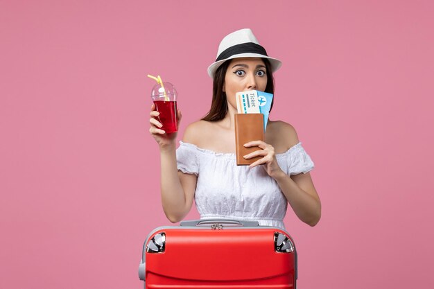 Vista frontal joven sosteniendo boletos con jugo de vacaciones en la pared rosa claro viaje de verano mujer viaje descanso