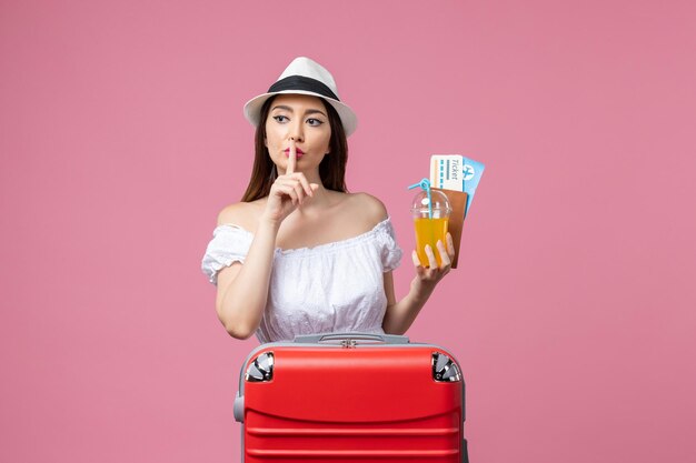 Vista frontal joven sosteniendo boletos para vacaciones y posando en la pared rosada vacaciones avión verano emoción viaje viaje
