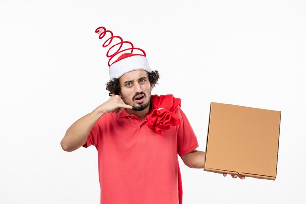 Vista frontal del joven sosteniendo la caja de comida de entrega en la pared blanca