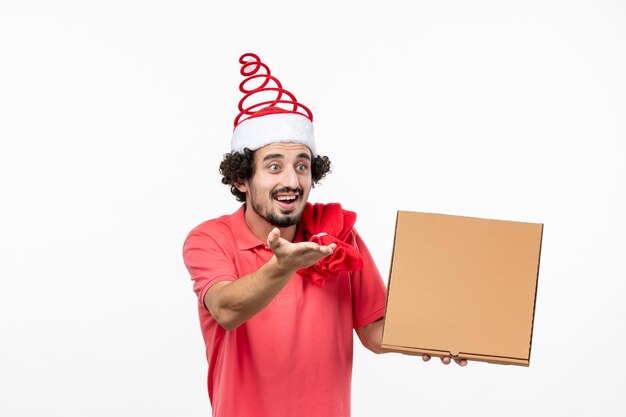 Vista frontal del joven sosteniendo la caja de comida de entrega en la pared blanca