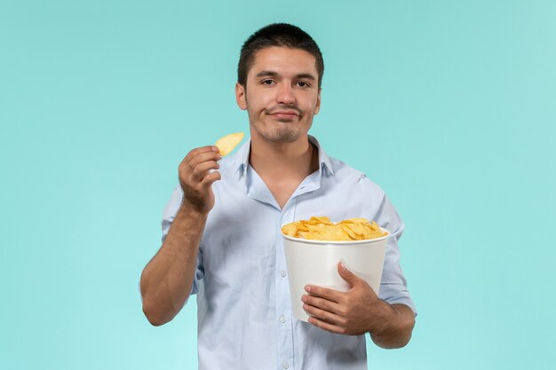 Vista frontal joven sosteniendo la canasta con cips comiendo en la pared azul película película remota cine macho