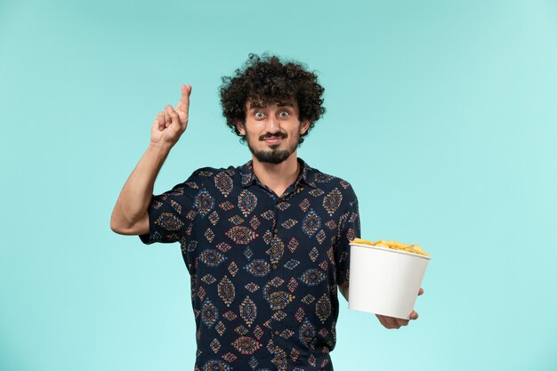 Vista frontal joven sosteniendo la canasta con cips y cruzando los dedos sobre la pared azul películas de cine remoto