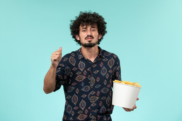 Vista frontal joven sosteniendo la canasta con cips en una pared azul película de películas de cine remoto