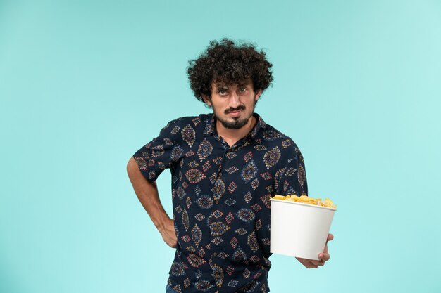 Vista frontal joven sosteniendo la canasta con cips en la pared azul películas de cine remoto películas