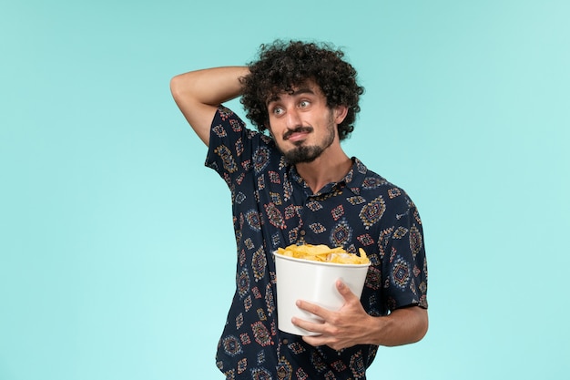 Vista frontal joven sosteniendo la canasta con cips pensando en la pared azul película cine cine teatro remoto